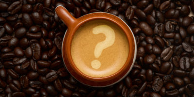Overhead shot of a coffee cup surrounded by a background of coffee beans with a question mark shown on the coffee