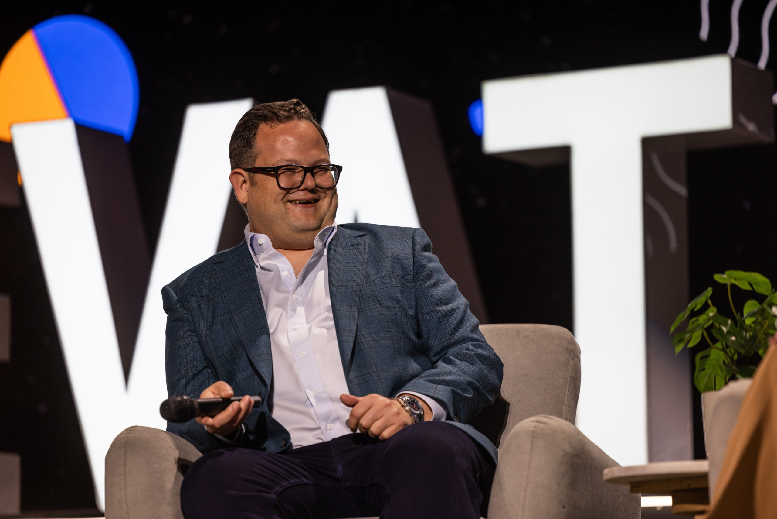 Person in a suit sitting in a chain with handheld microphone