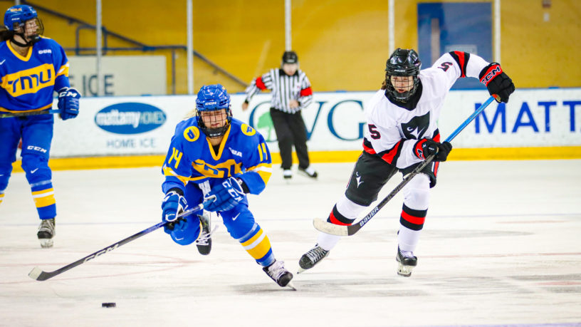 TMU Bold women's hockey player Megan Bergmanis and a Carleton Ravens player chase after a loose puck