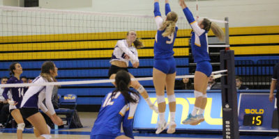 Two players from the TMU women's volleyball team jump to try to block a spike from the Western Mustangs