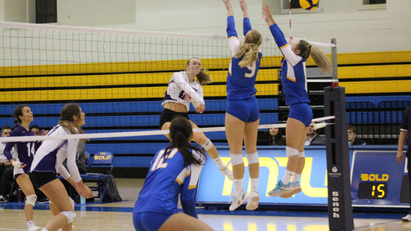 Two players from the TMU women's volleyball team jump to try to block a spike from the Western Mustangs