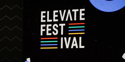 Sign reads "Elevate Festival" on stage with black backdrop.