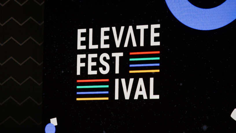 Sign reads "Elevate Festival" on stage with black backdrop.