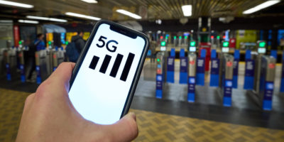 A person holds a phone with a 5G symbol on it's screen while in front of ticket gates in a TTC subway station