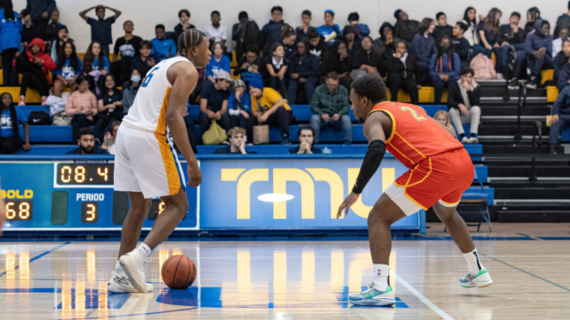 TMU men's basketball player David Walker dribbles the basketball past half-court while being guarded by a Calgary Dinos defender