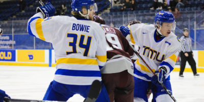 Two TMU men's hockey players battle for a loose puck against a Ottawa Gee-Gees player