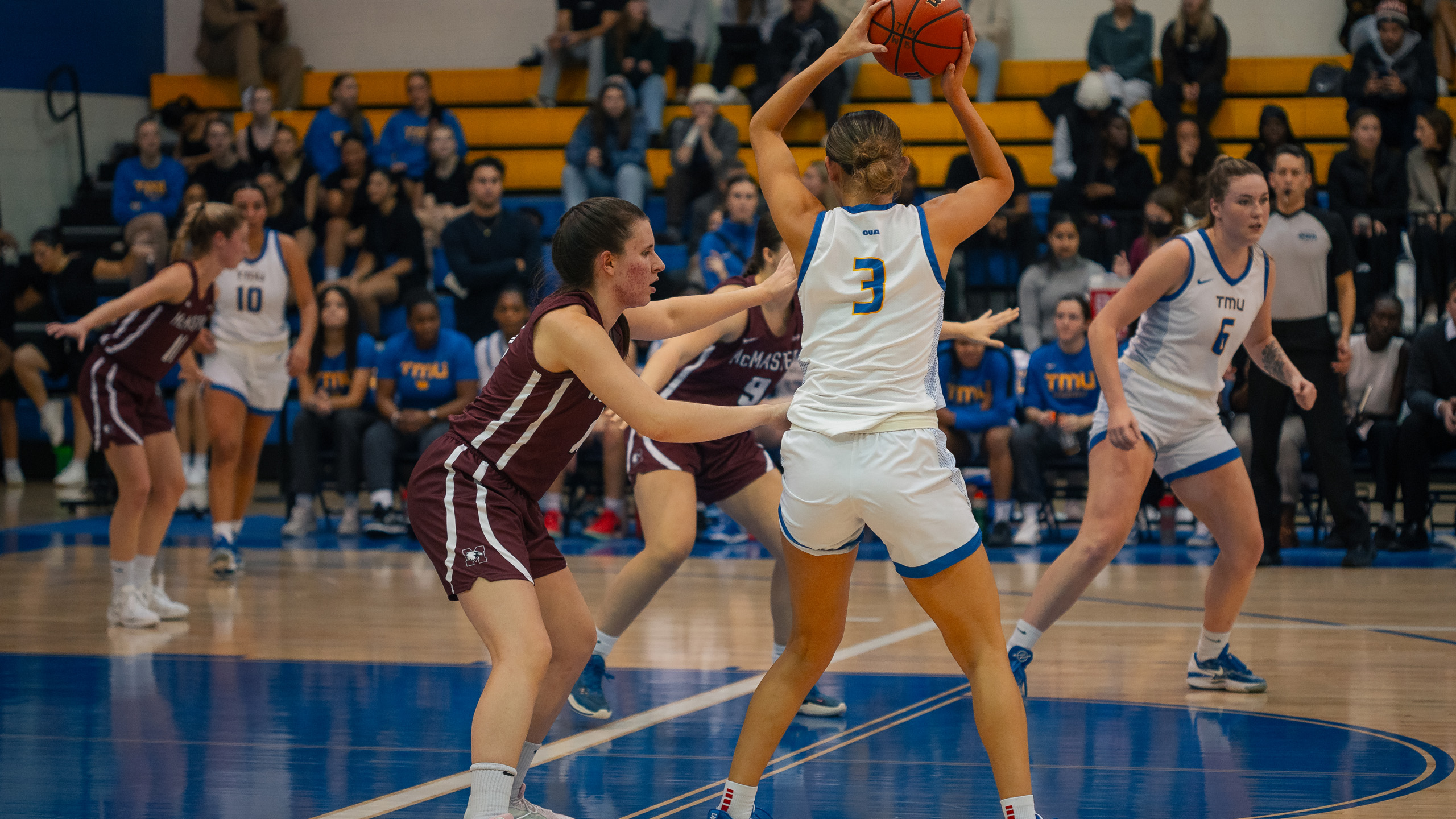 TMU women's basketball player Hailey Franco-DeRyck holds the balls above her head as she's guarded by a McMaster Marauders player
