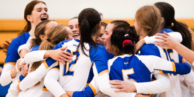 The TMU women's volleyball team huddle in celebration of a win