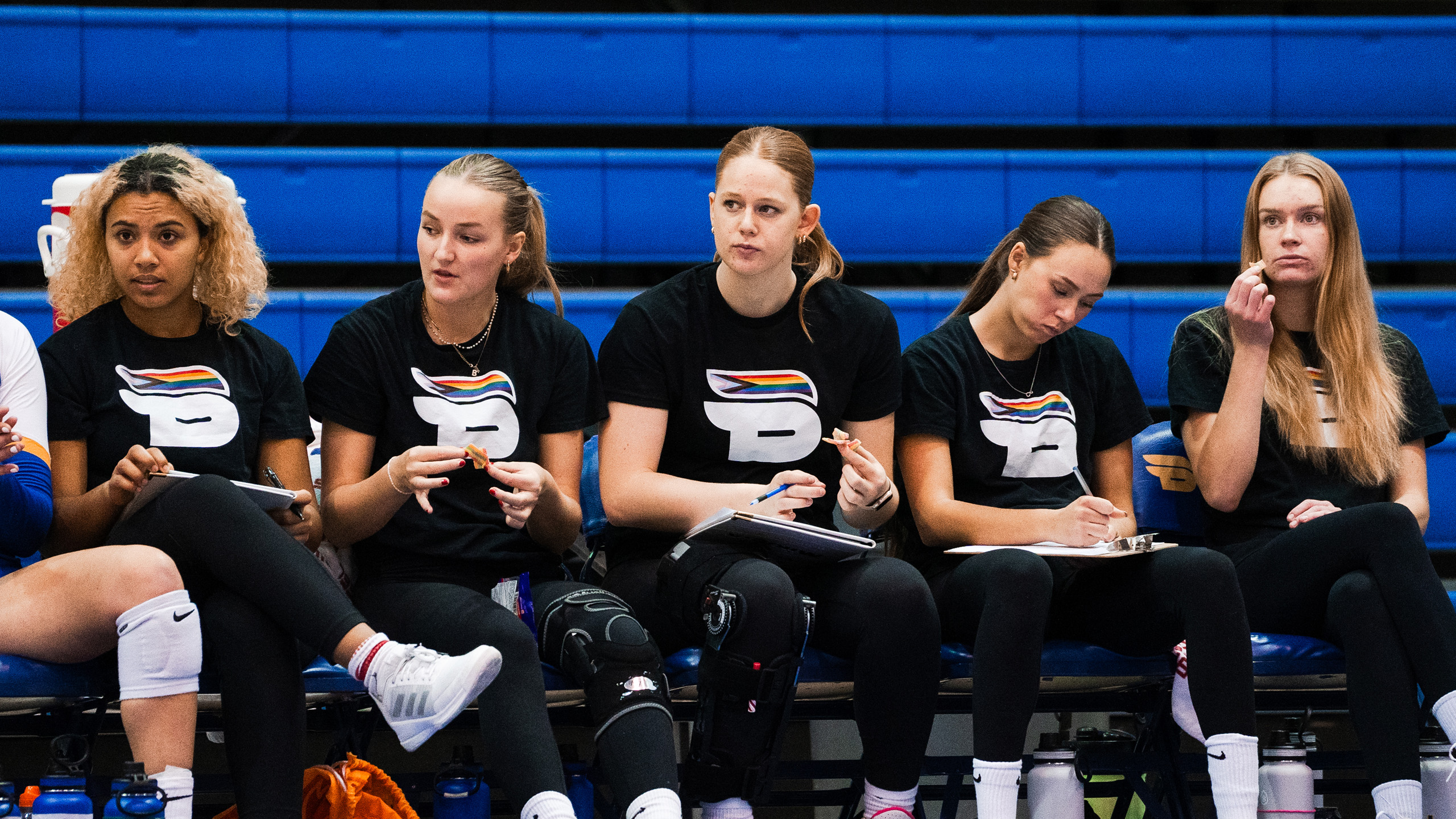 TMU women's volleyball players wear the Bold pride shirt while sitting on the bench