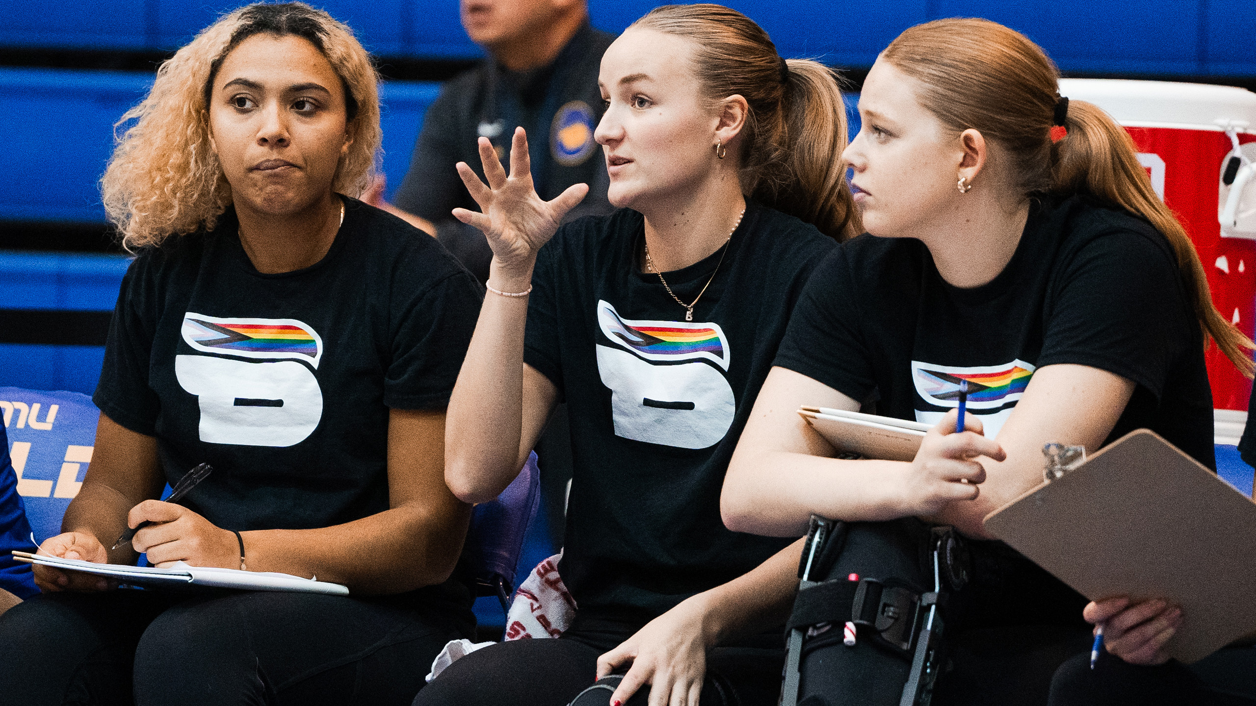 TMU women's volleyball players Maya Griffith, Britney Veltman and Darcie Buchanan sit on the bench while wearing the Bold Pride shirt