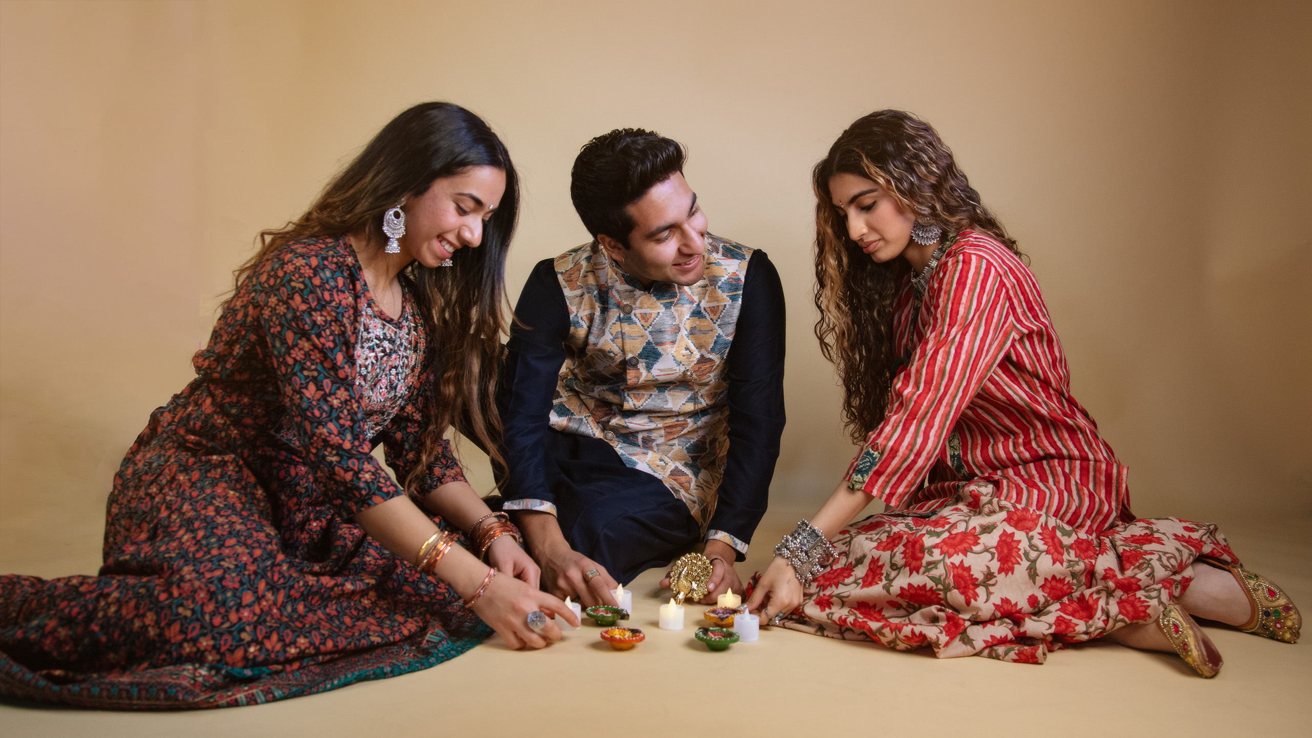 Three people arranging diyas and smiling at each other