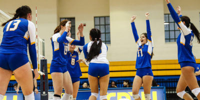 TMU women's volleyball players throw their hands in the air in celebration of scoring a point