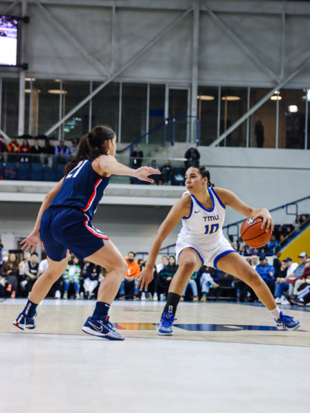 TMU women's basketball player Jayme Foreman dribbles the ball while being guarded by UConn Huskies player Inês Bettencourt