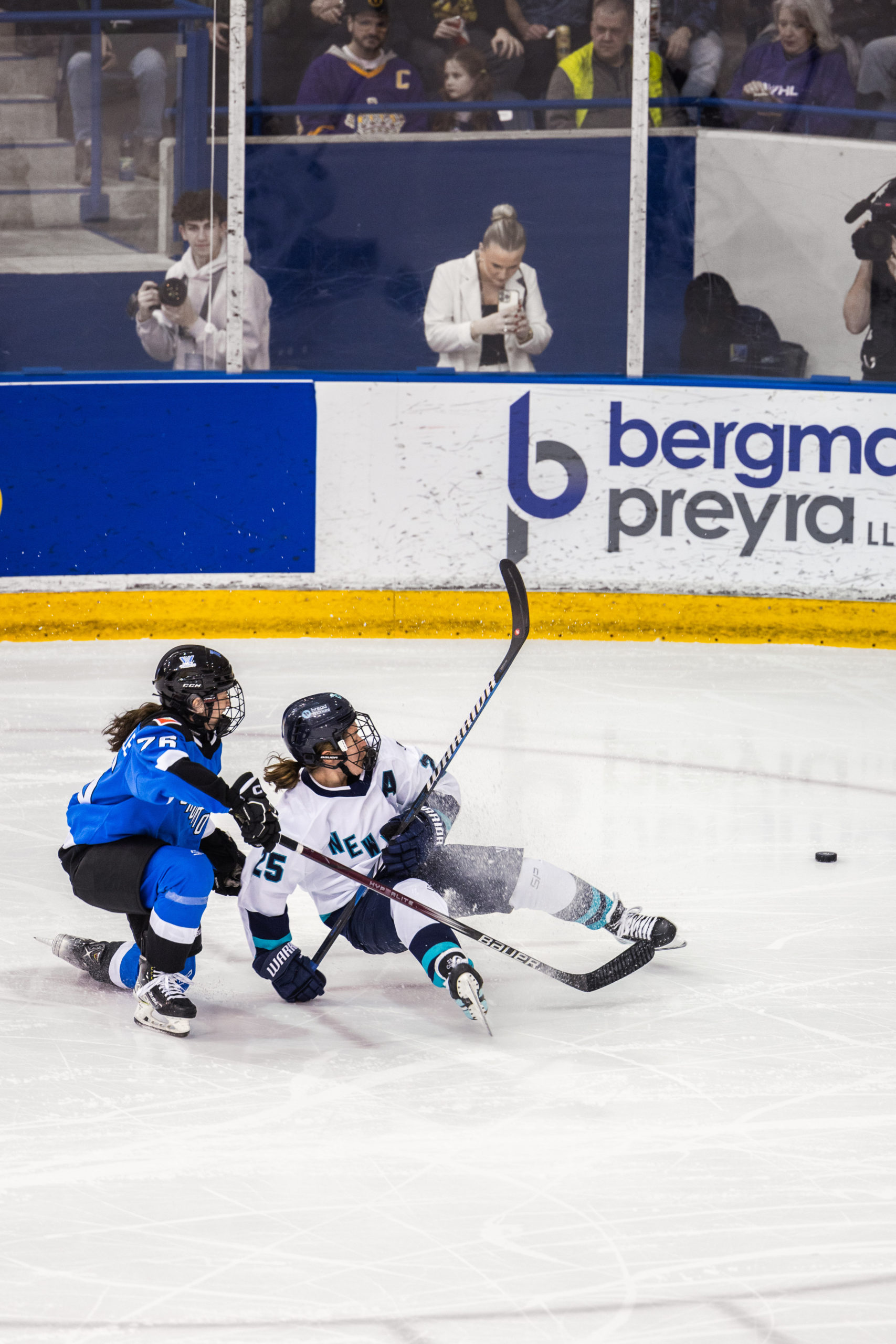 PWHL Toronto and PWHL Boston players fall to the ground as they fight for the puck