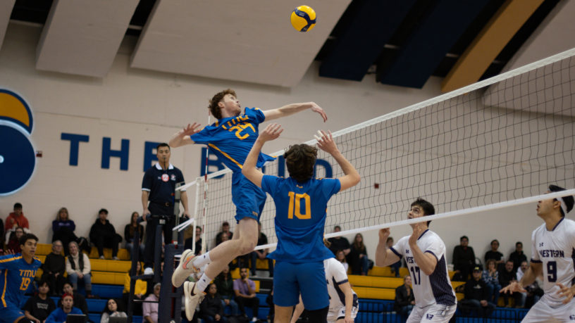 TMU men's volleyball player Liam Cobb spikes the ball over the net against the Western Mustangs