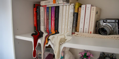 A bookshelf with books and a camera. The bottoms of the books are melting off the shelf.