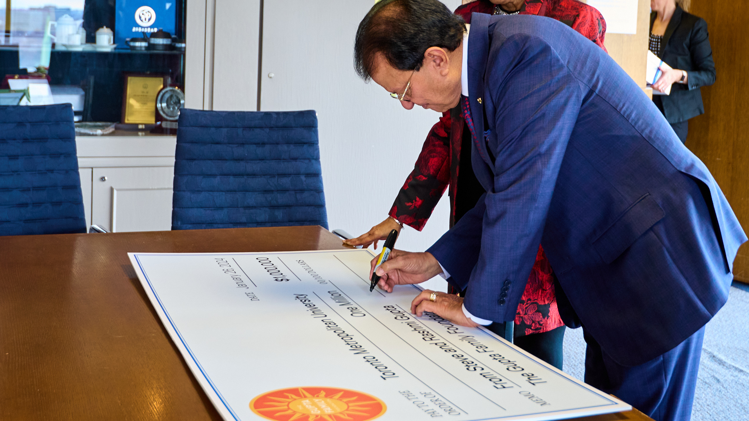 Man signing cheque with Sharpie marker. Large cheque placed on table.