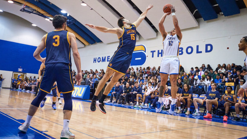 TMU Bold men's basketball player Aaron Rhooms shoots over a Queen's player