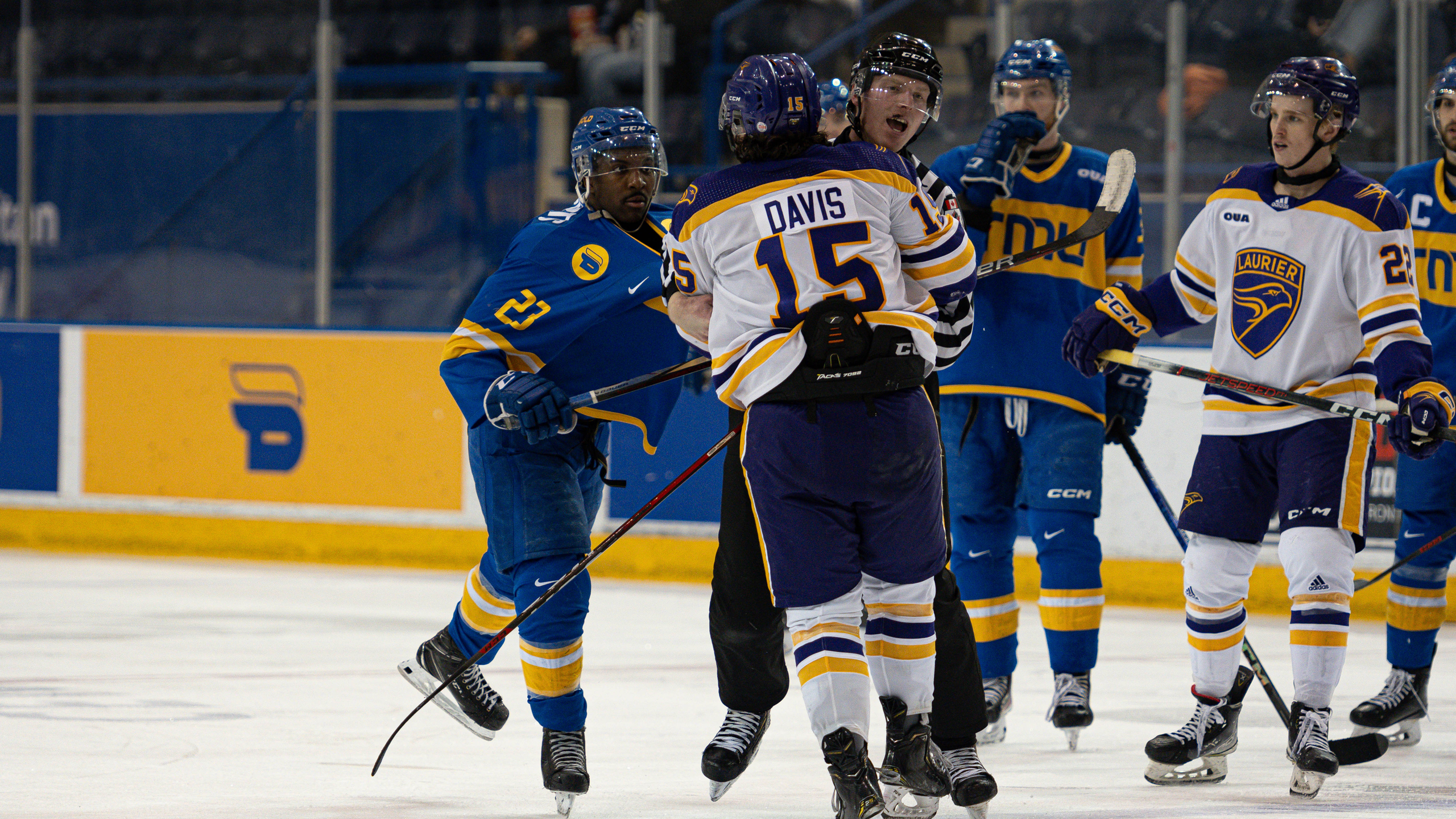 A referee holds back Wilfrid Laurier Golden Hawks player Tyler Davis as he fights some TMU players