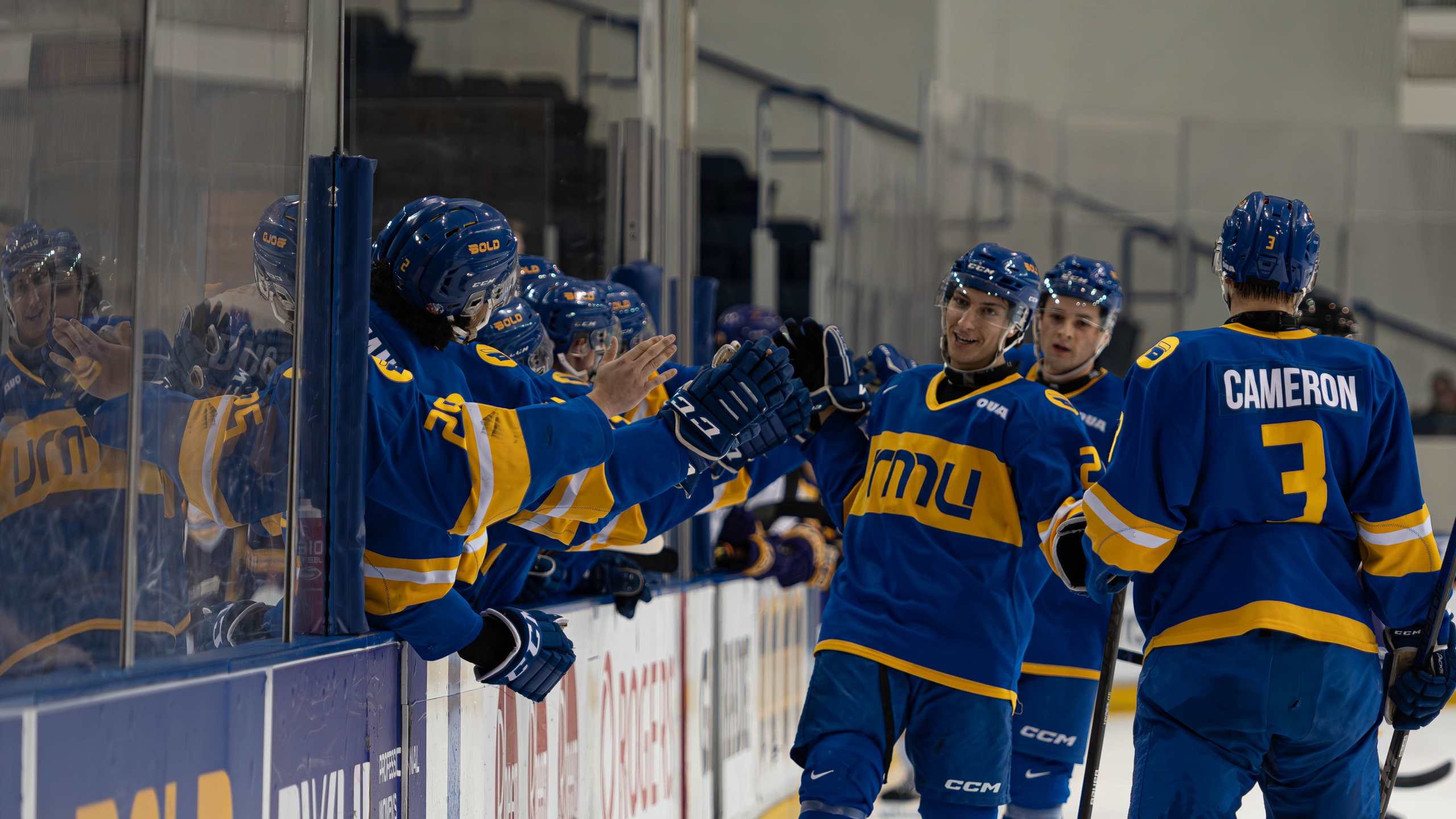 Members of the TMU Bold men's hockey team skate and high five their teammates on the bench