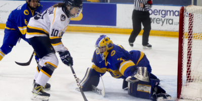 A member of the Windsor Lancers women's hockey team skates to the net with the puck as she faces the TMU Bold women's hockey goalie