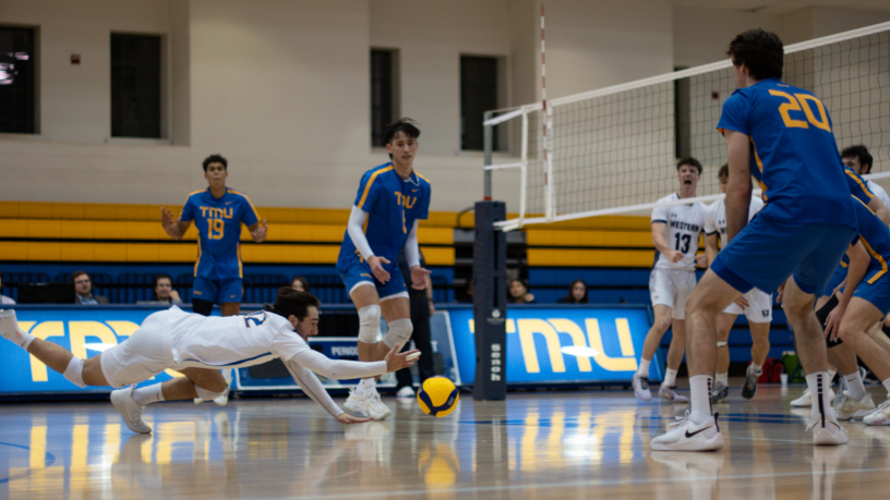 TMU Bold men's volleyball player Tony Tanouchev dives to hit the ball as his teammates watch