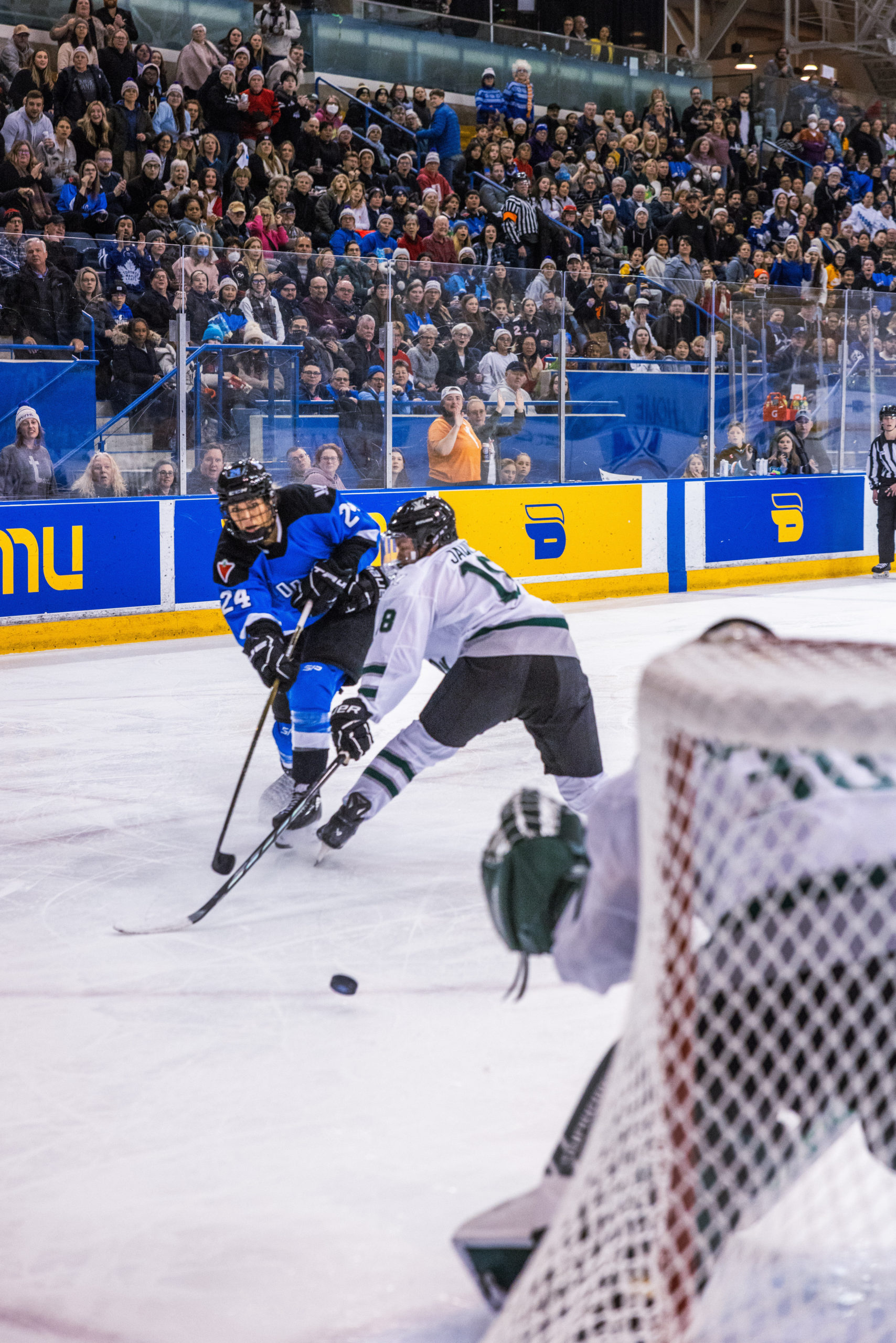 A PWHL Toronto player shoots the puck at the PWHL Boston goal