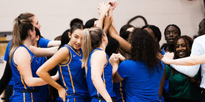 TMU women's basketball team huddle together with their fists in the air