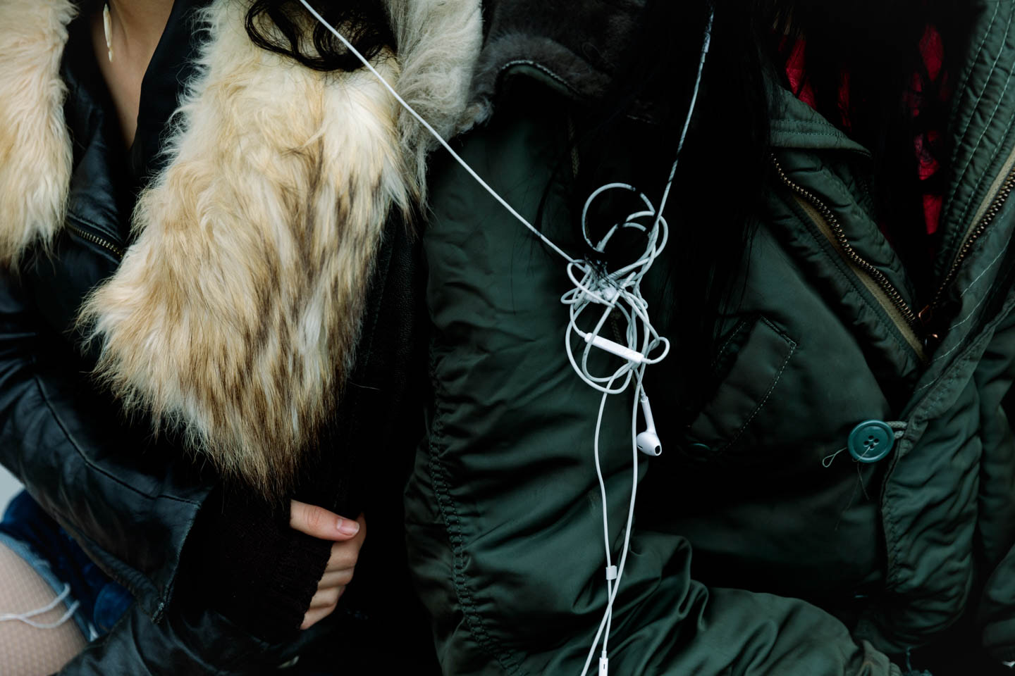 Two people sit together with tangled headphones in between them.