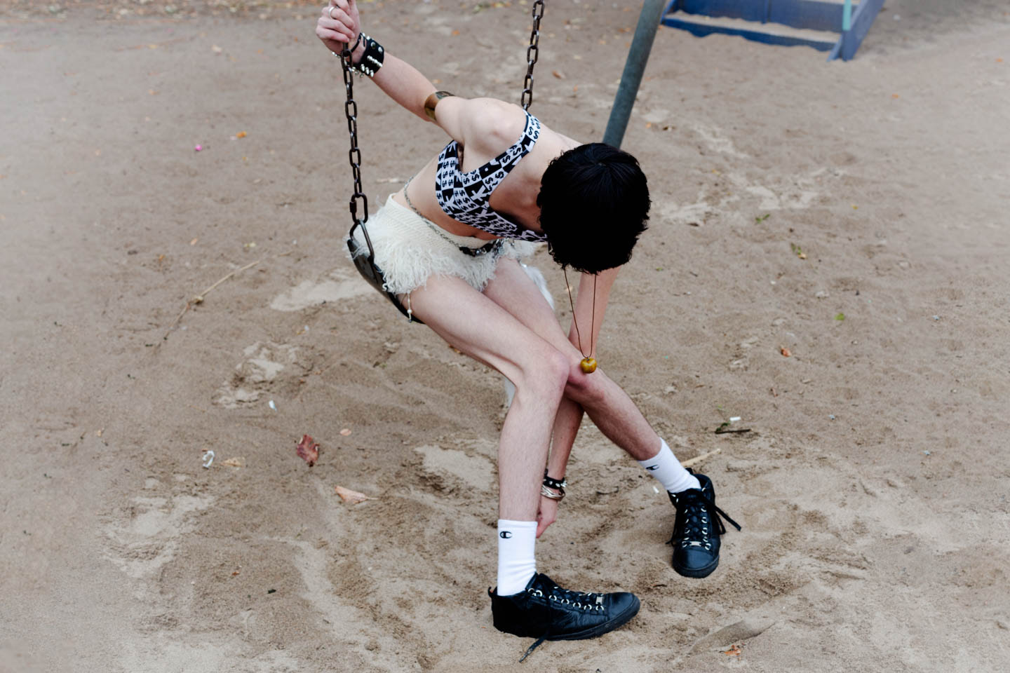 A person sits bent over on the swings in a sandpit as they adjust their socks.