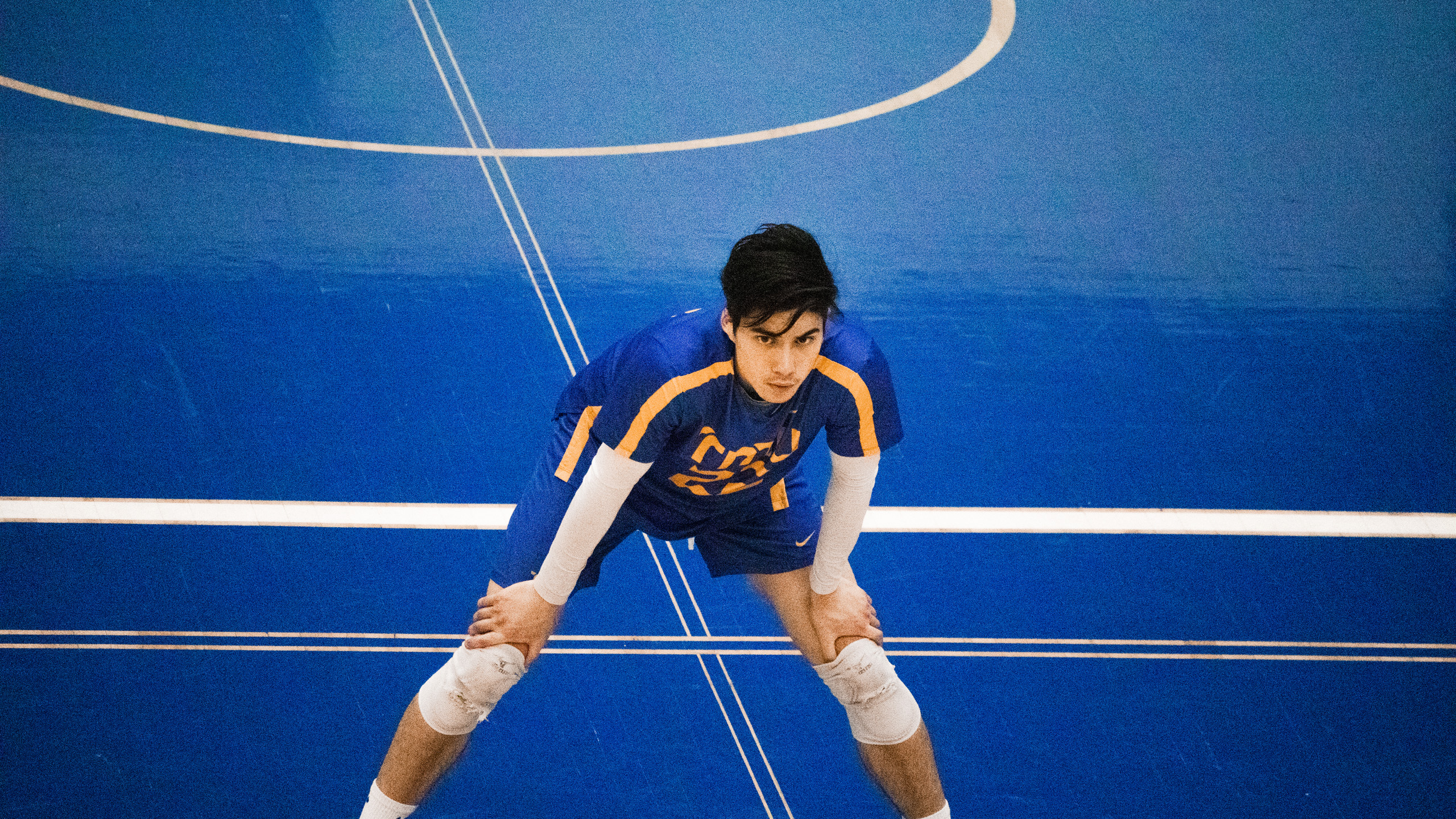 TMU men's volleyball player Lucas Yang hunches over on the court with his hands on his knees