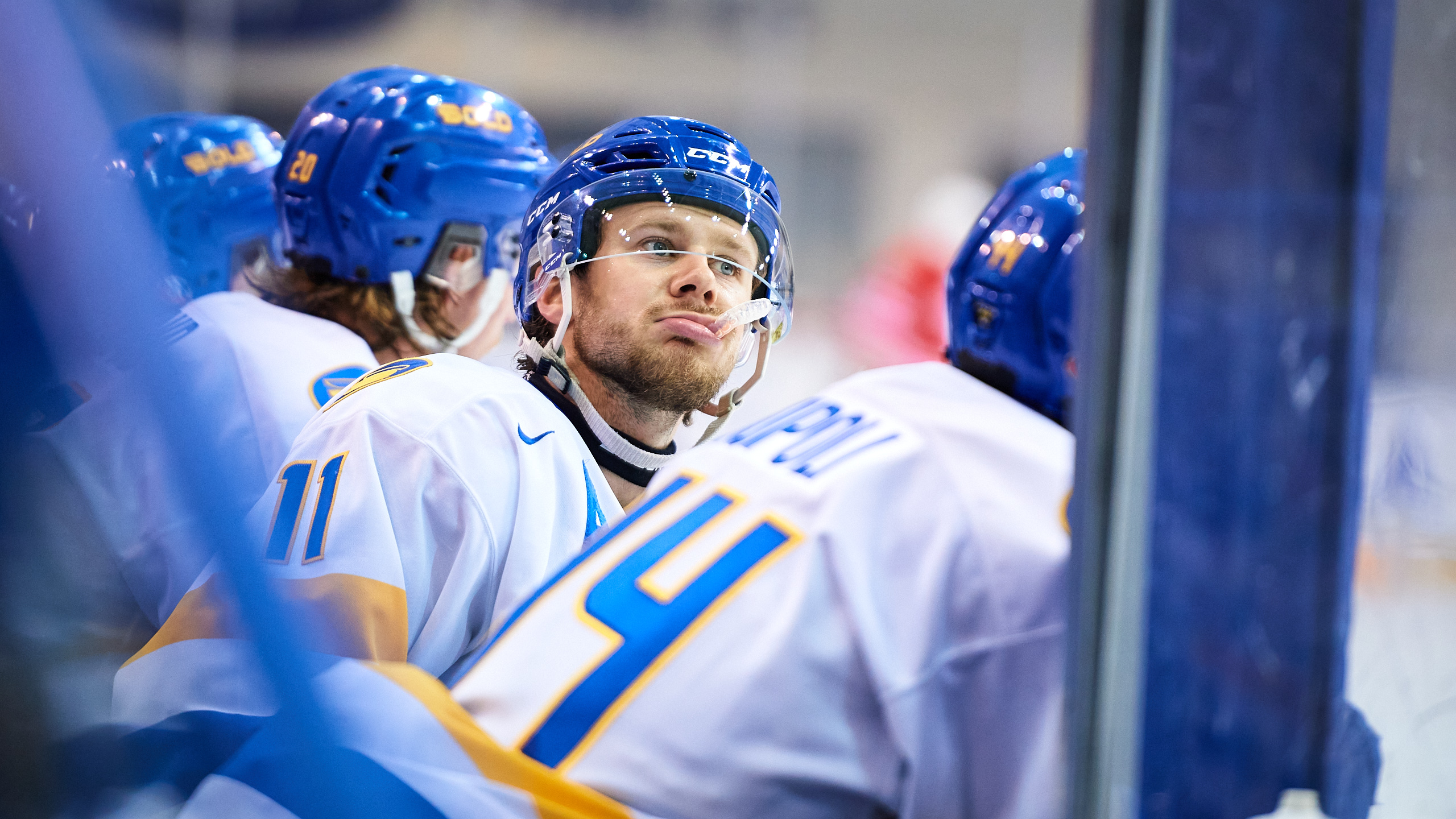 TMU men's hockey player Ryan Wells stares at the ice while on the bench with his mouthguard hanging out of his mouth
