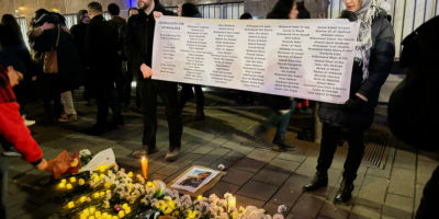 a poster with names is held up by two people at a vigil