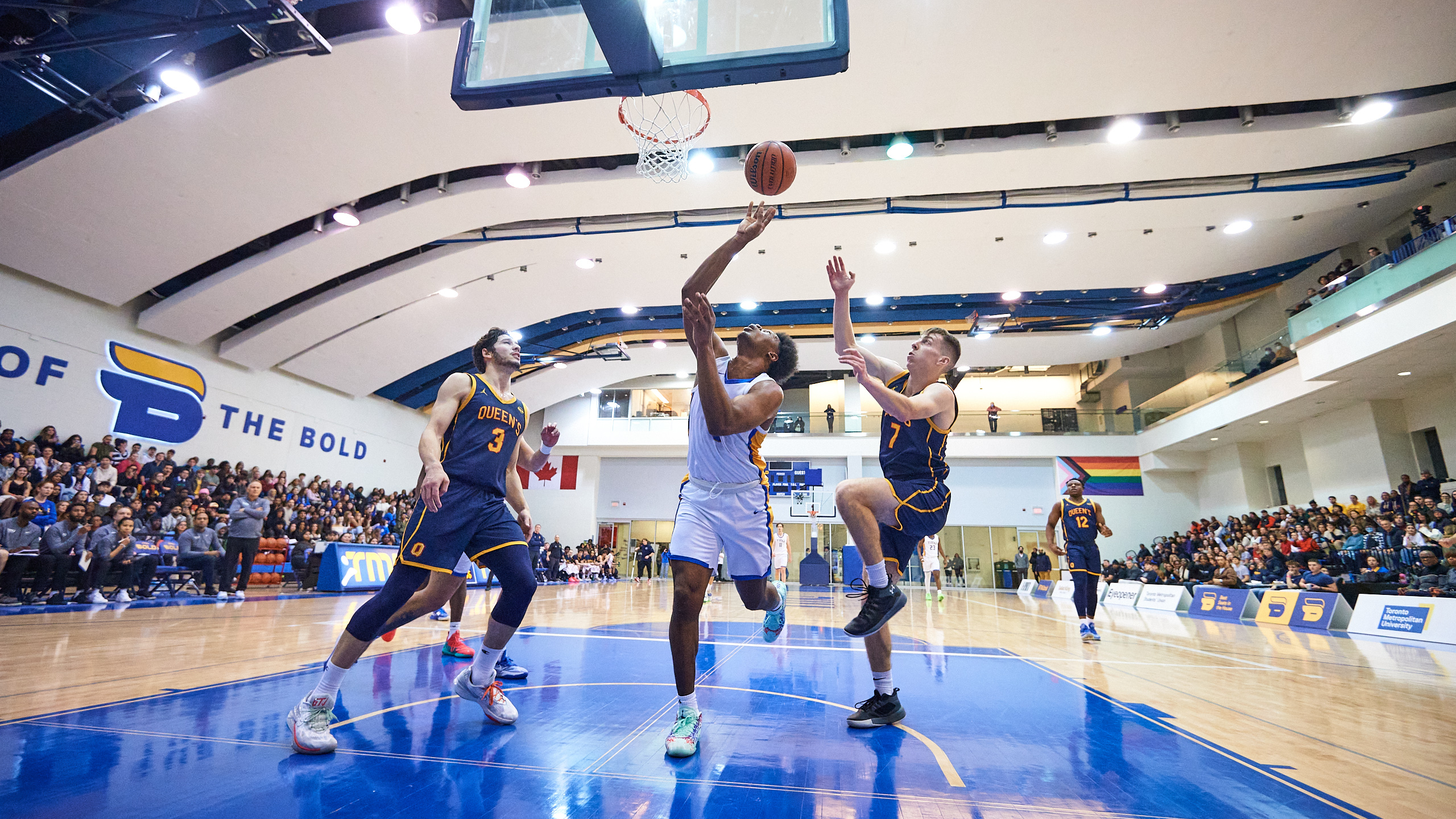 TMU men's basketball player David Walker goes for a layup in between two Queen's players
