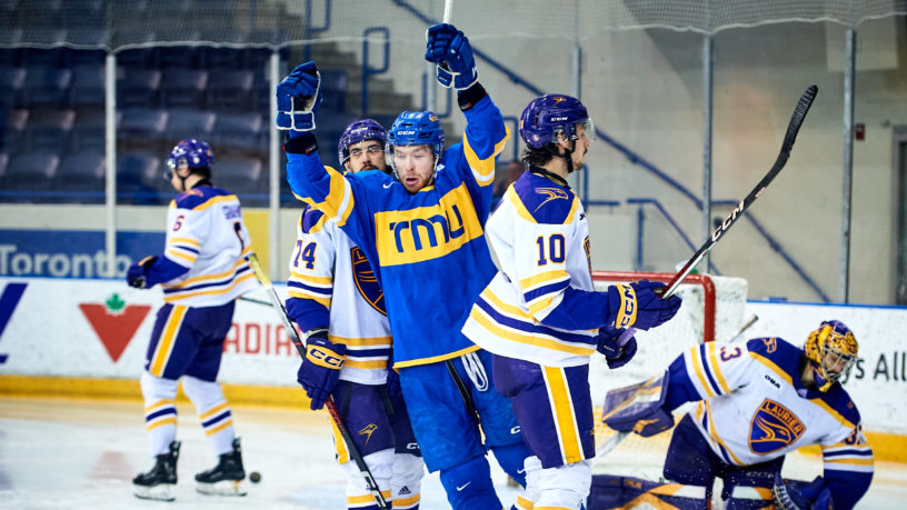 TMU men's ice hockey player Connor Bowie celebrates a goal in front of four Golden Hawks players