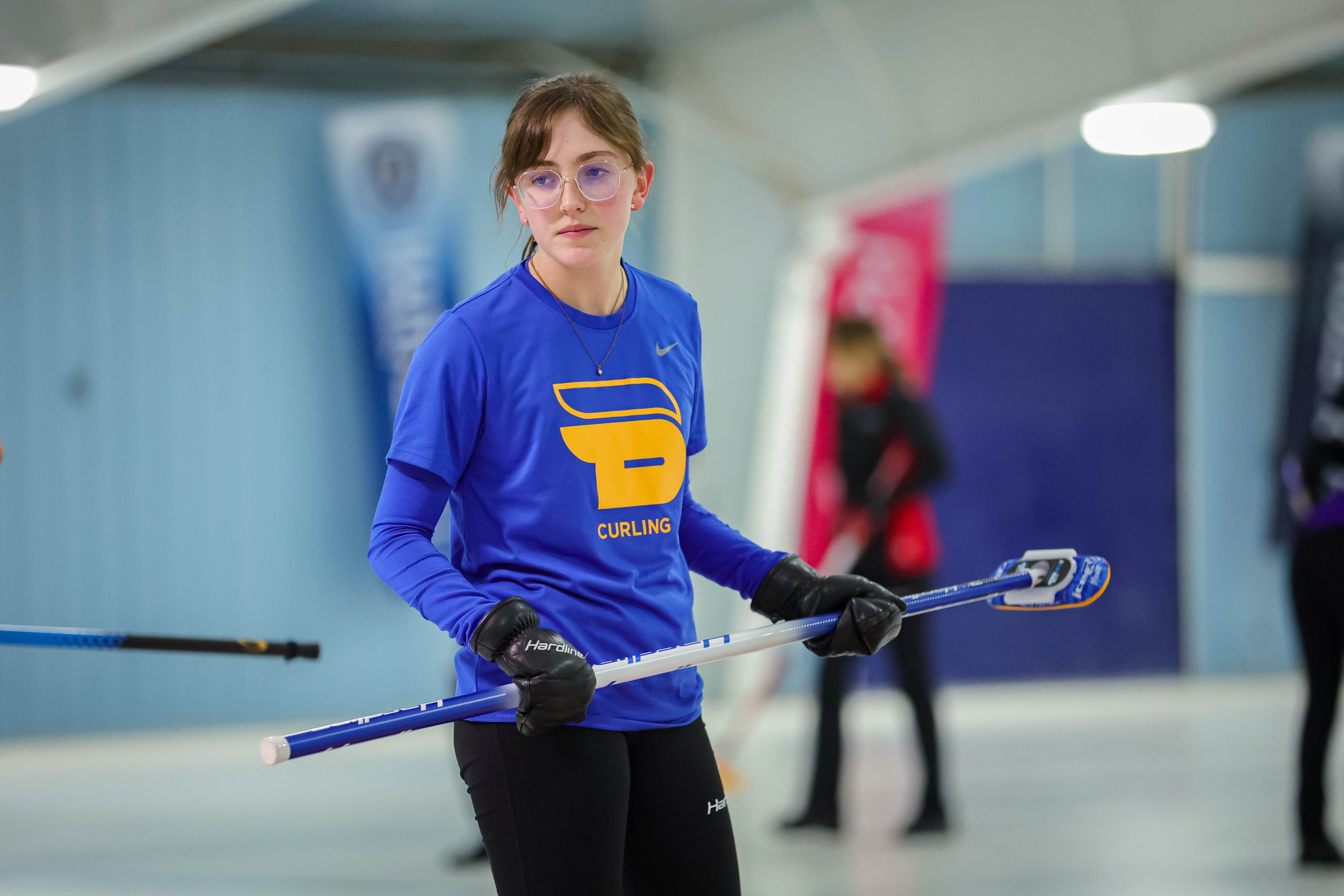 A TMU women's curling player stands with a broom on the ice