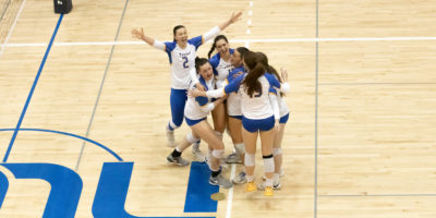 Members of the TMU Bold women's volleyball team celebrate on court after their win over the Western Mustangs
