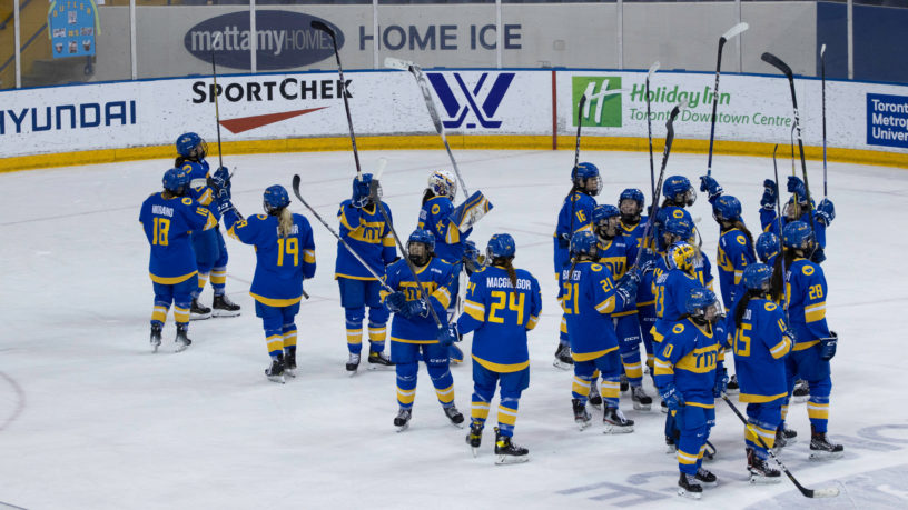 Members of the TMU Bold women's hockey team hold their sticks in the air to celebrate their win