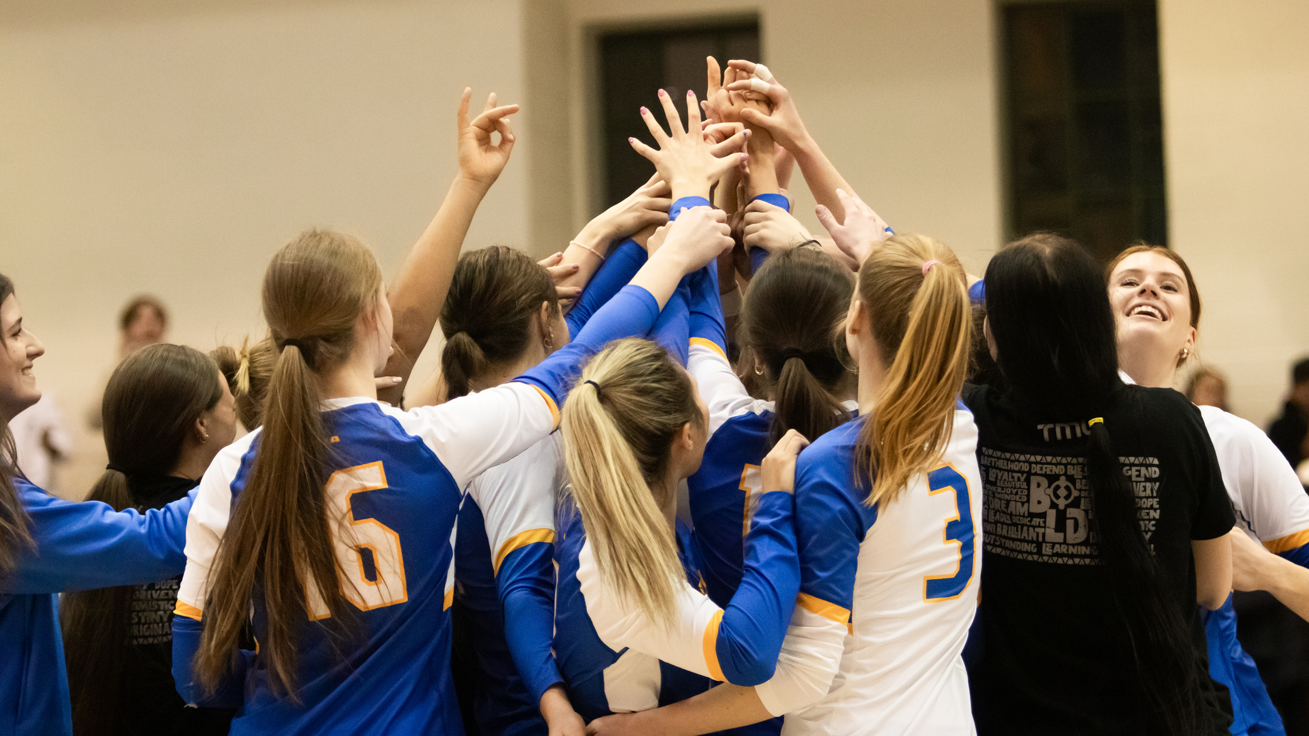 Members of the TMU Bold women's volleybal team put their hands in a circle to celebrate their win