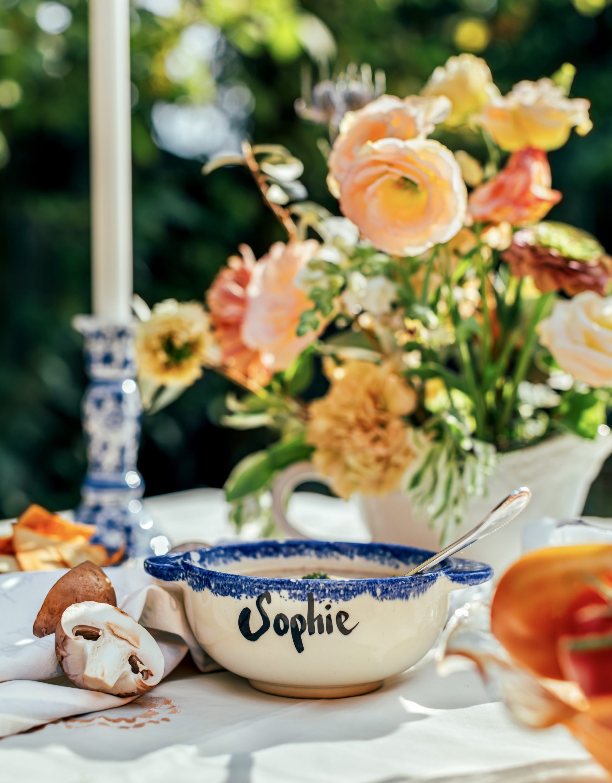 A white bowl with a blue rim design lays in the center of a table surrounded by various ingredients and centerpieces. The text on the blow reads "Sophie"