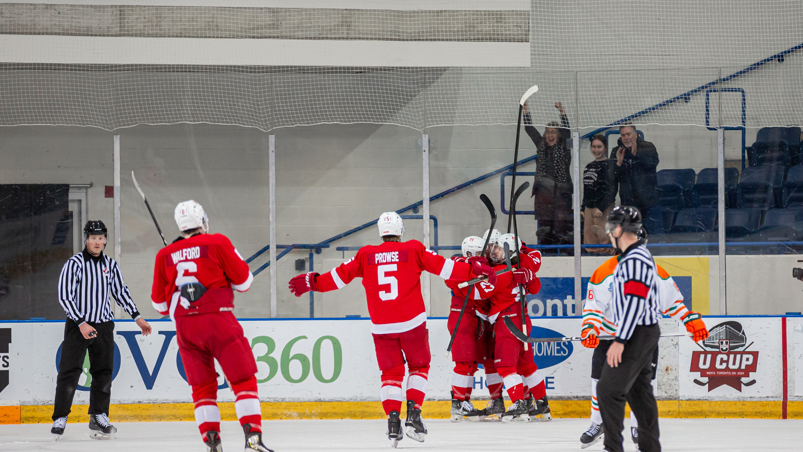 Two McGill Redbirds skate towards a group of three teammates celebrating a goal