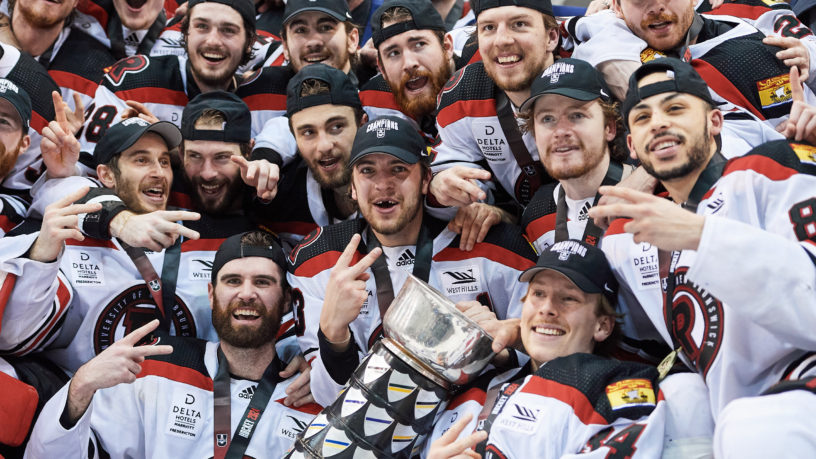 Players from the UNB Reds yell with the U Cup in the middle of them in celebration of the win