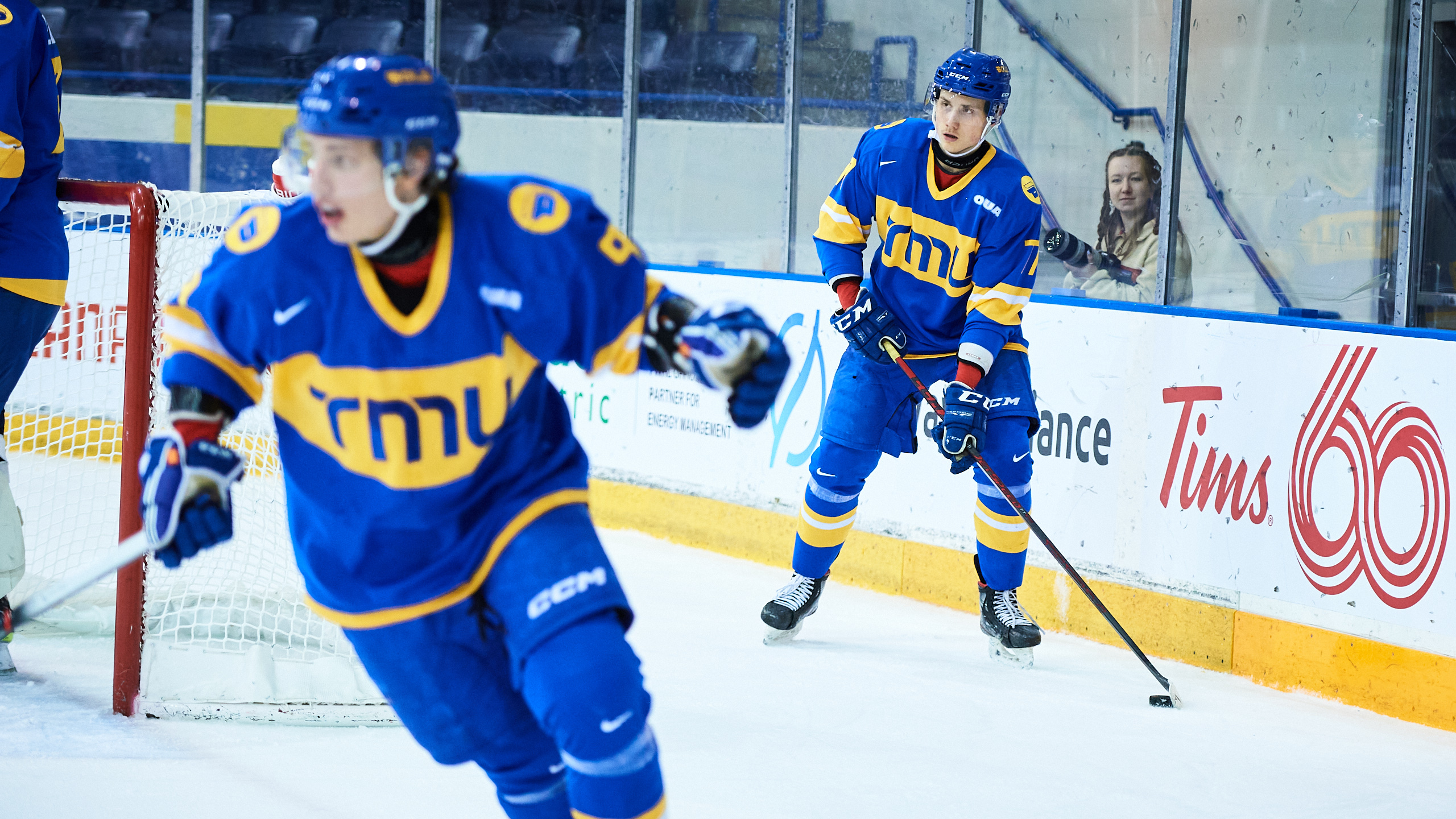 TMU men's hockey player Artem Duda skates with the puck behind the goal as Daniil Grigorev skates forward