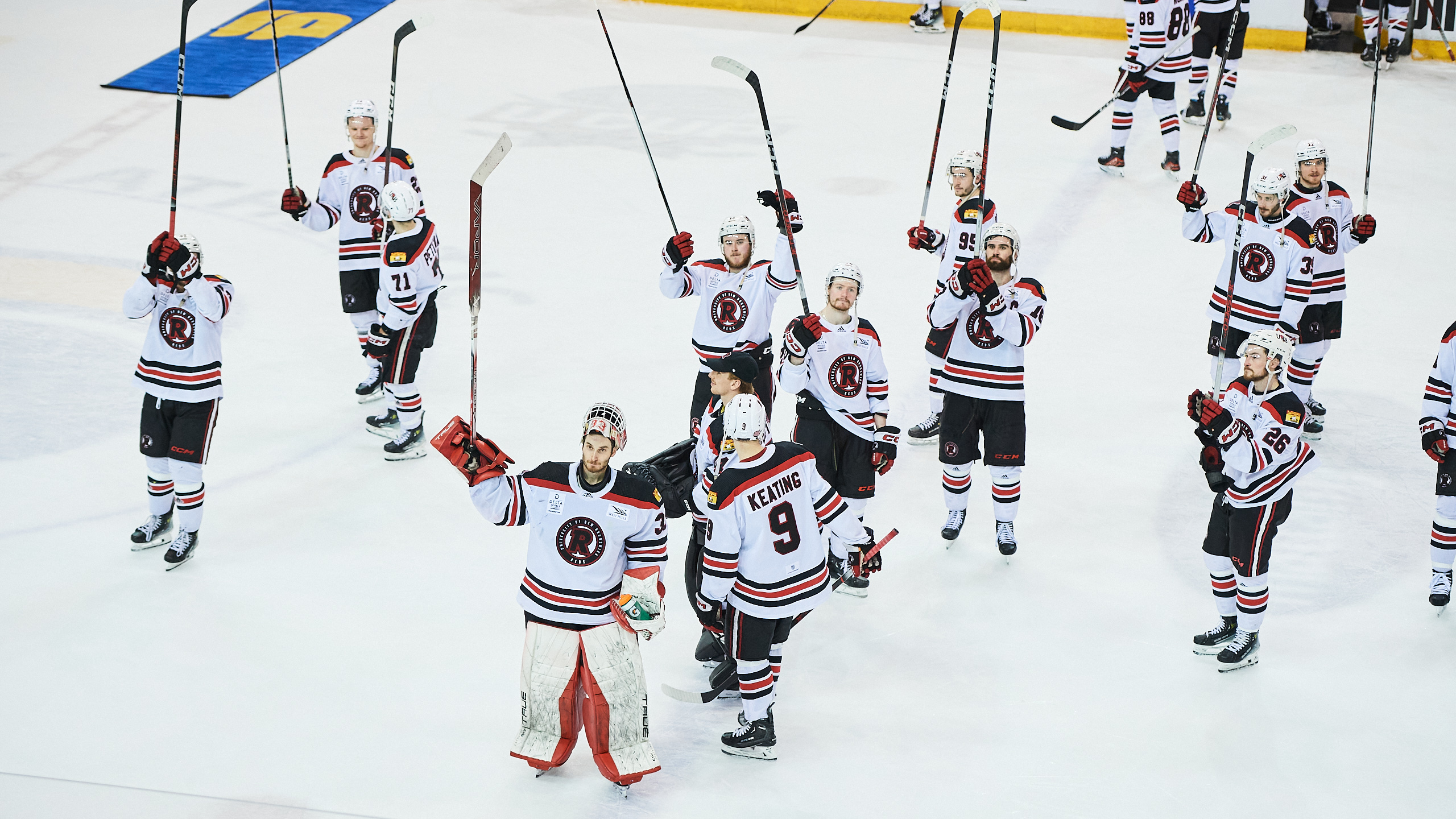 UNB Reds players celebrate the win lifting their sticks in the air