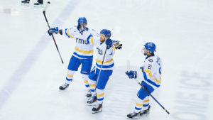 TMU Bold men's hockey player Carson Gallagher celebrates his goal with two teammates beside him