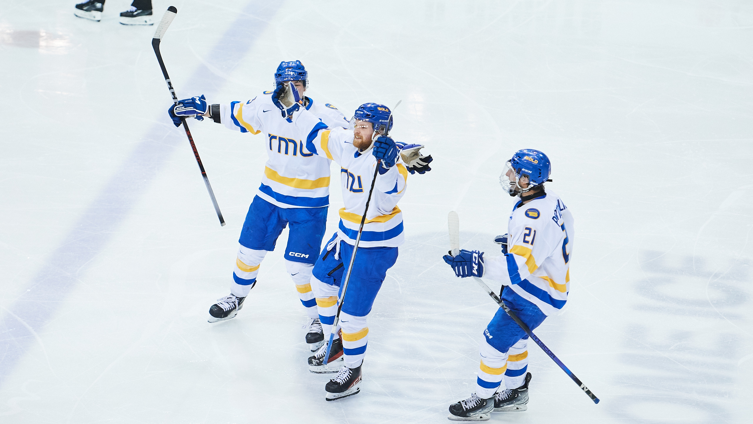 TMU Bold men's hockey player Carson Gallagher celebrates his goal with two teammates beside him