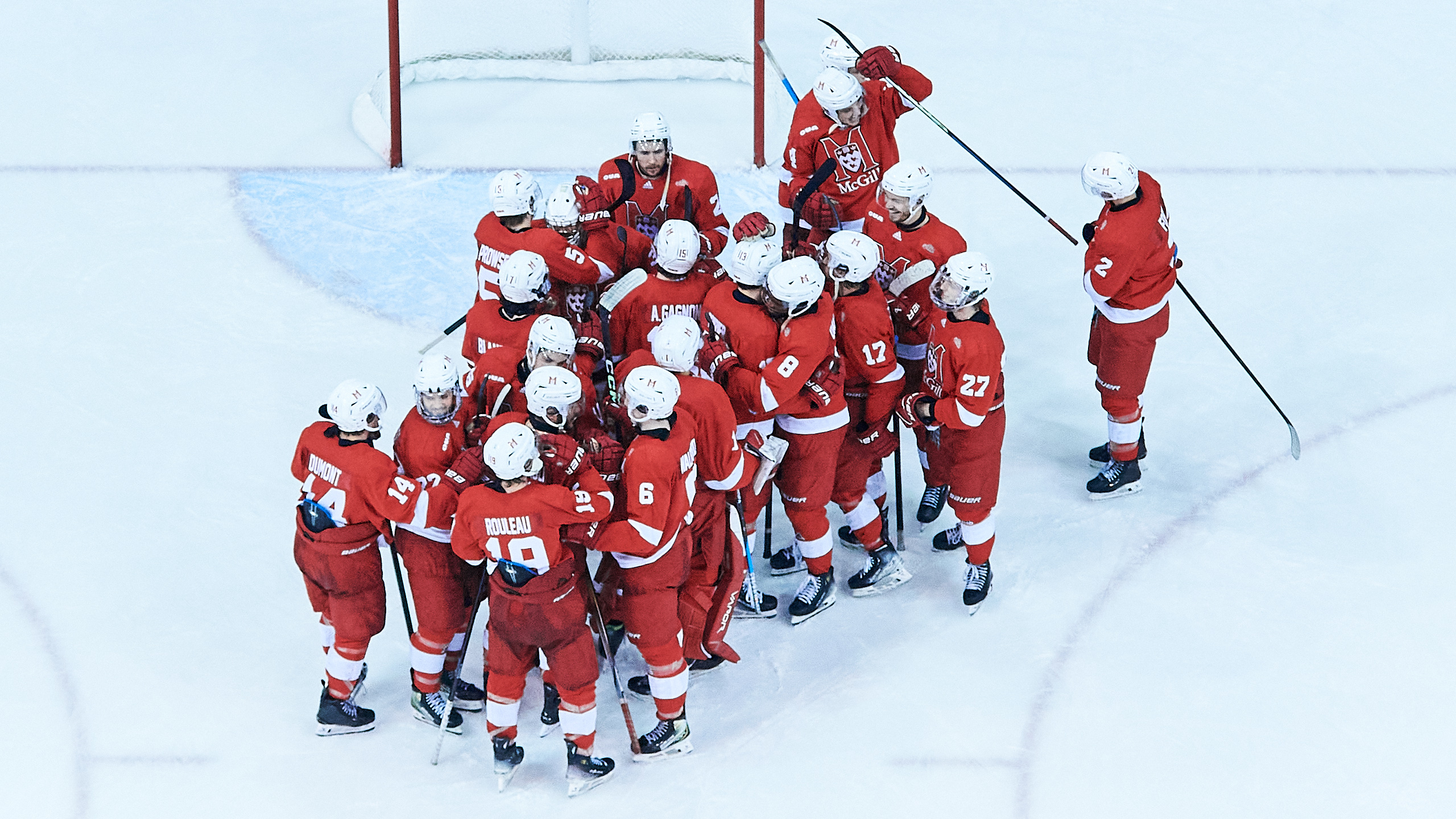 The McGill Redbirds men's hockey team huddle together on the ice after winning