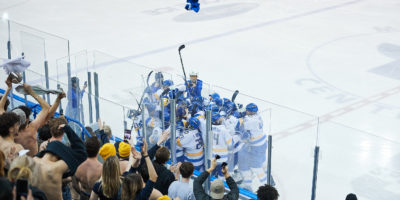 The TMU Bold men's hockey team celebrates their win in a huddle as the crowd cheers them on