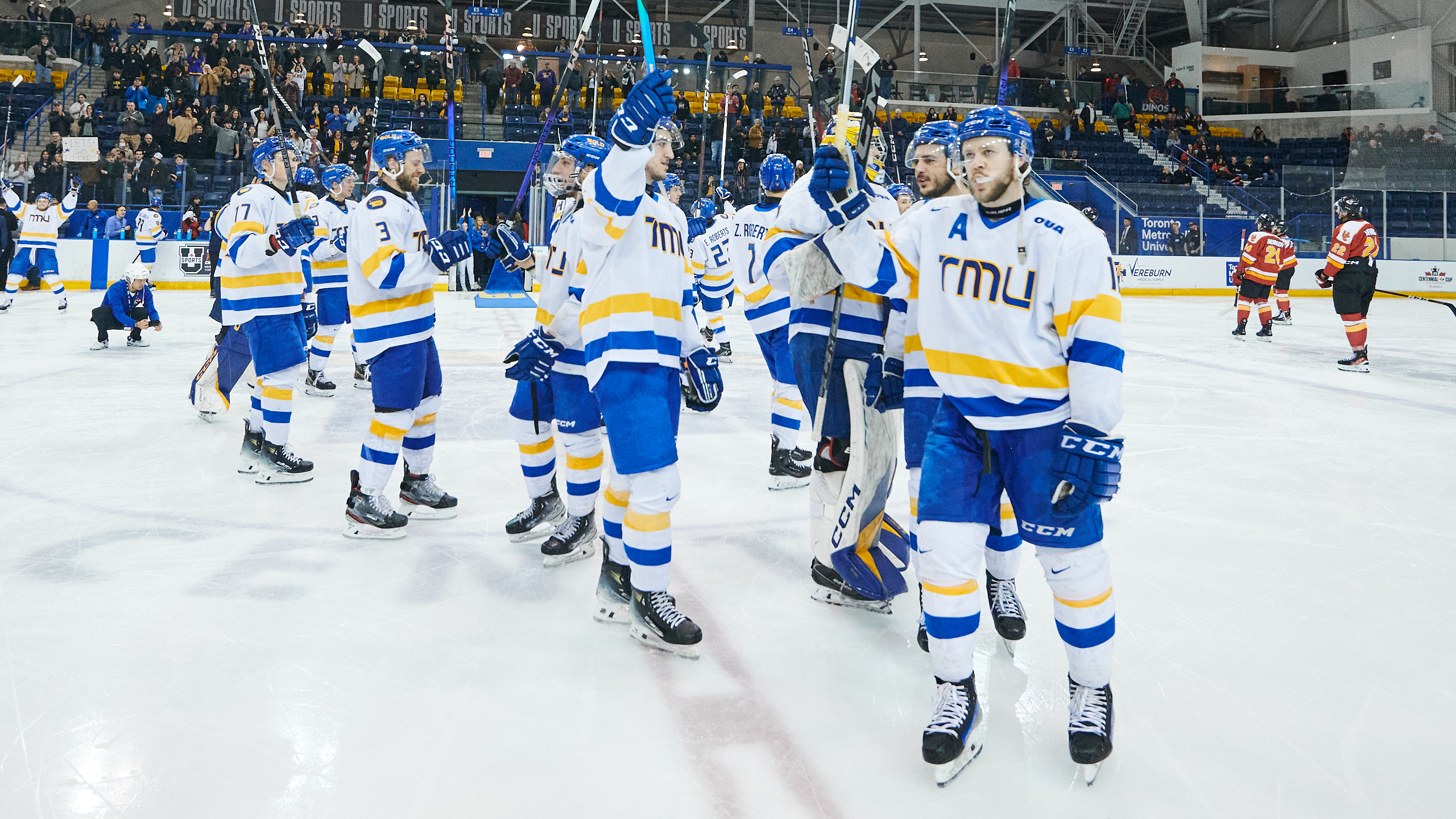 TMU Bold hockey players raise their sticks in celebration on the ice after their win