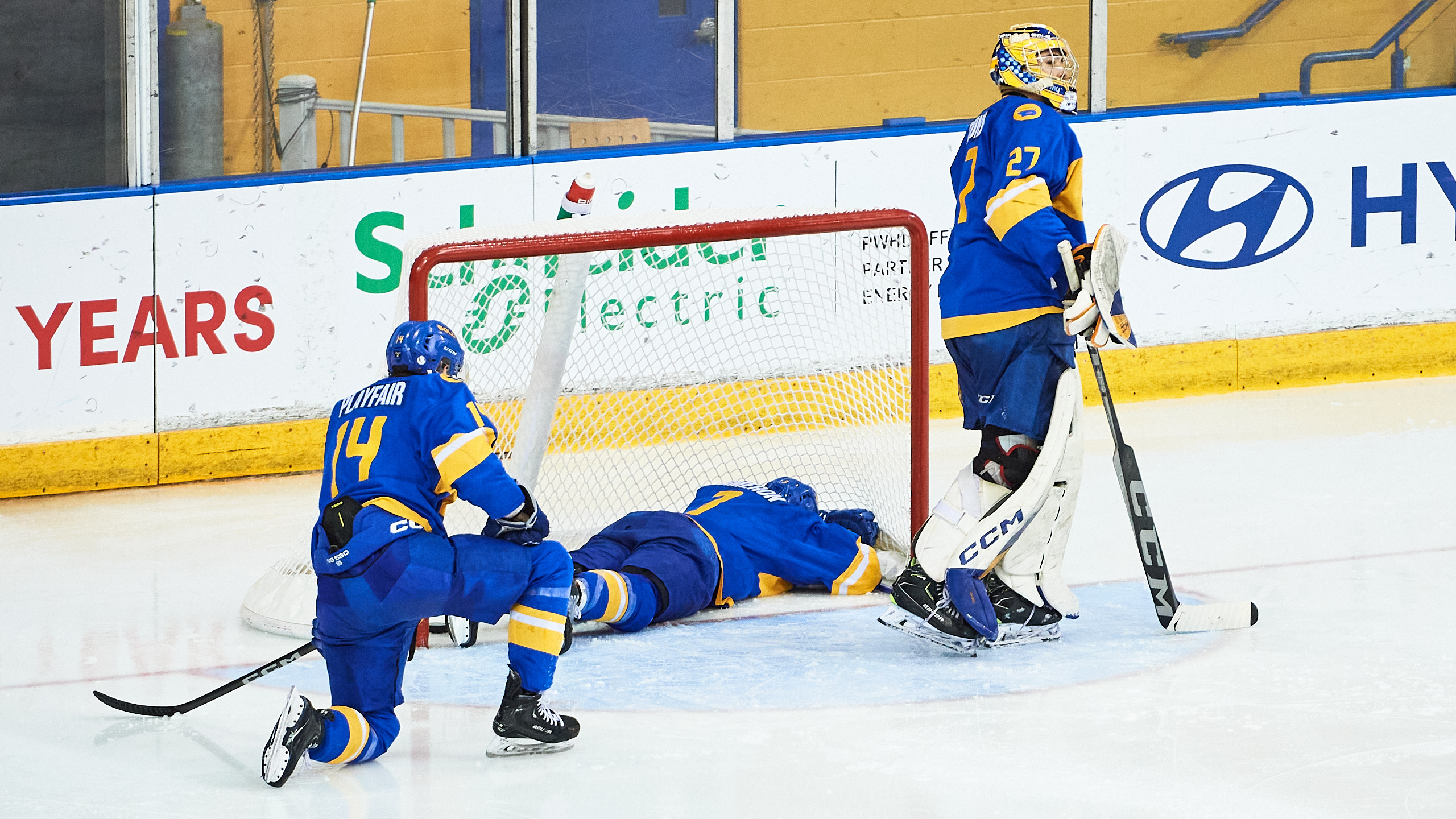 A TMU player lays face first in the net on the ice as one kneels and another skates off